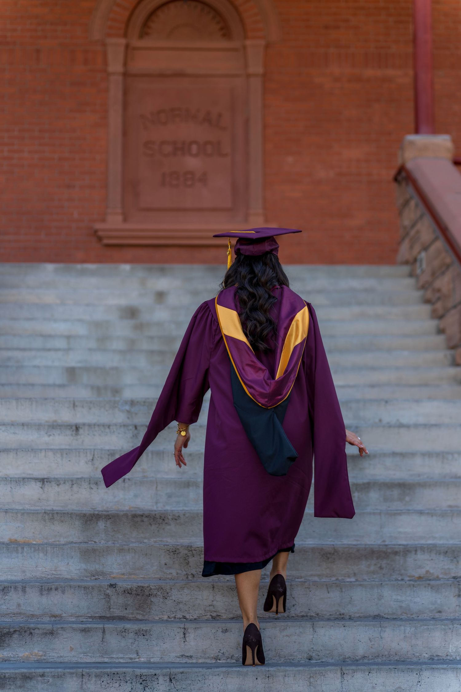Graduate walking up steps of historic 1894 school building in academic regalia.
