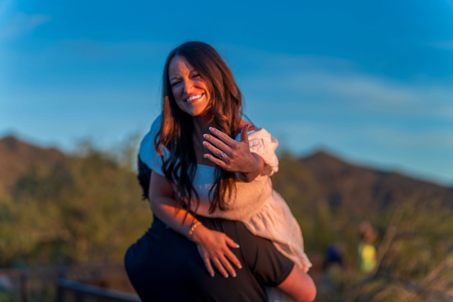 Two people embrace joyfully against a backdrop of desert mountains and blue sky.