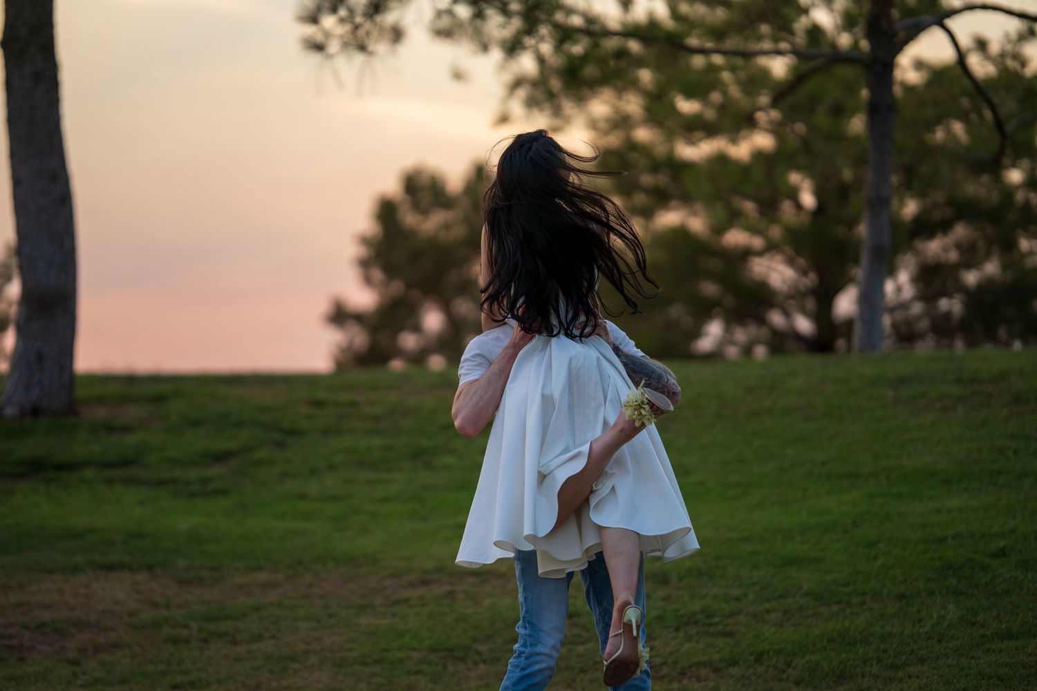 Woman in white dress spinning in a green park at sunset, hair flowing in the breeze.
