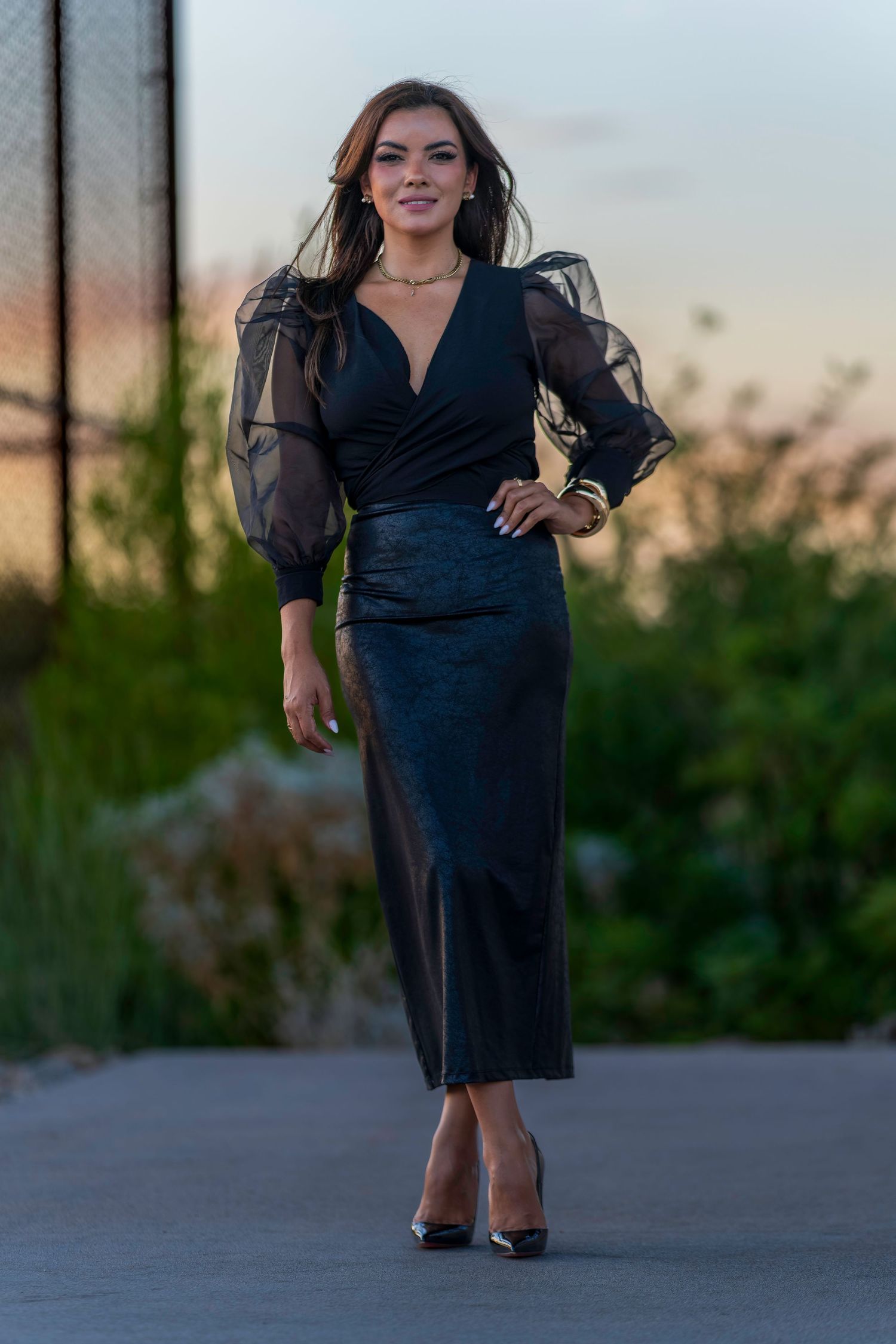 Woman in black sheer puff-sleeve midi dress walking confidently outdoors at dusk.