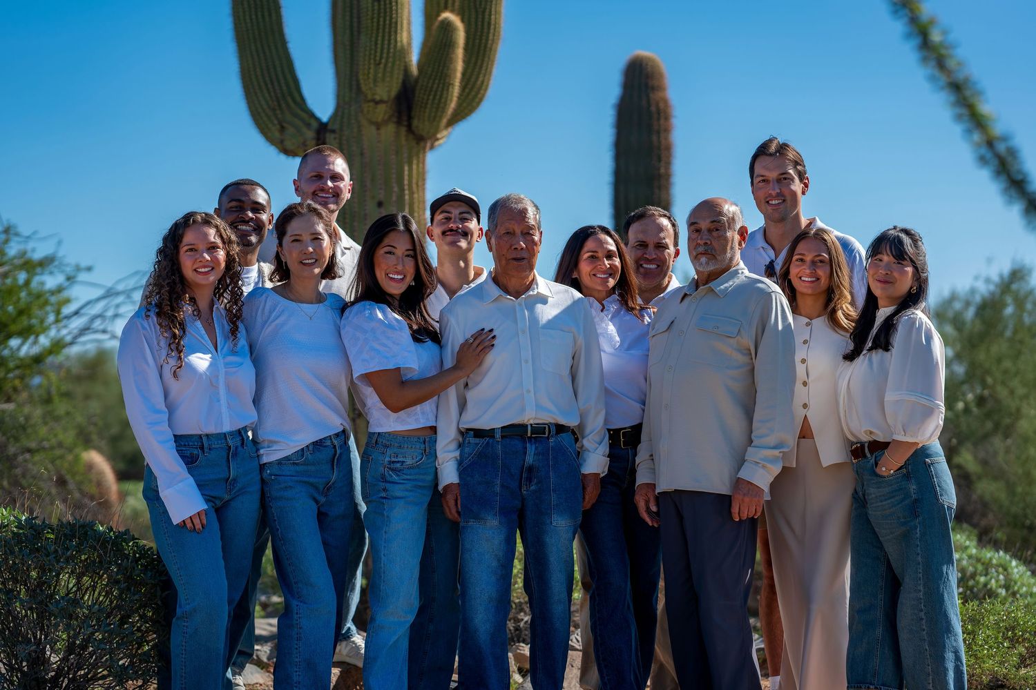 A group photo taken in front of tall saguaro cacti in the Arizona desert with matching outfits.