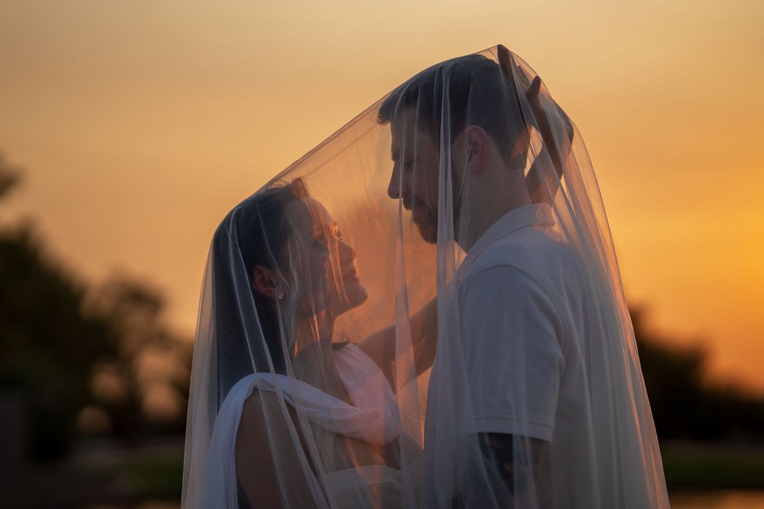 Romantic couple moment under flowing veil during golden hour.