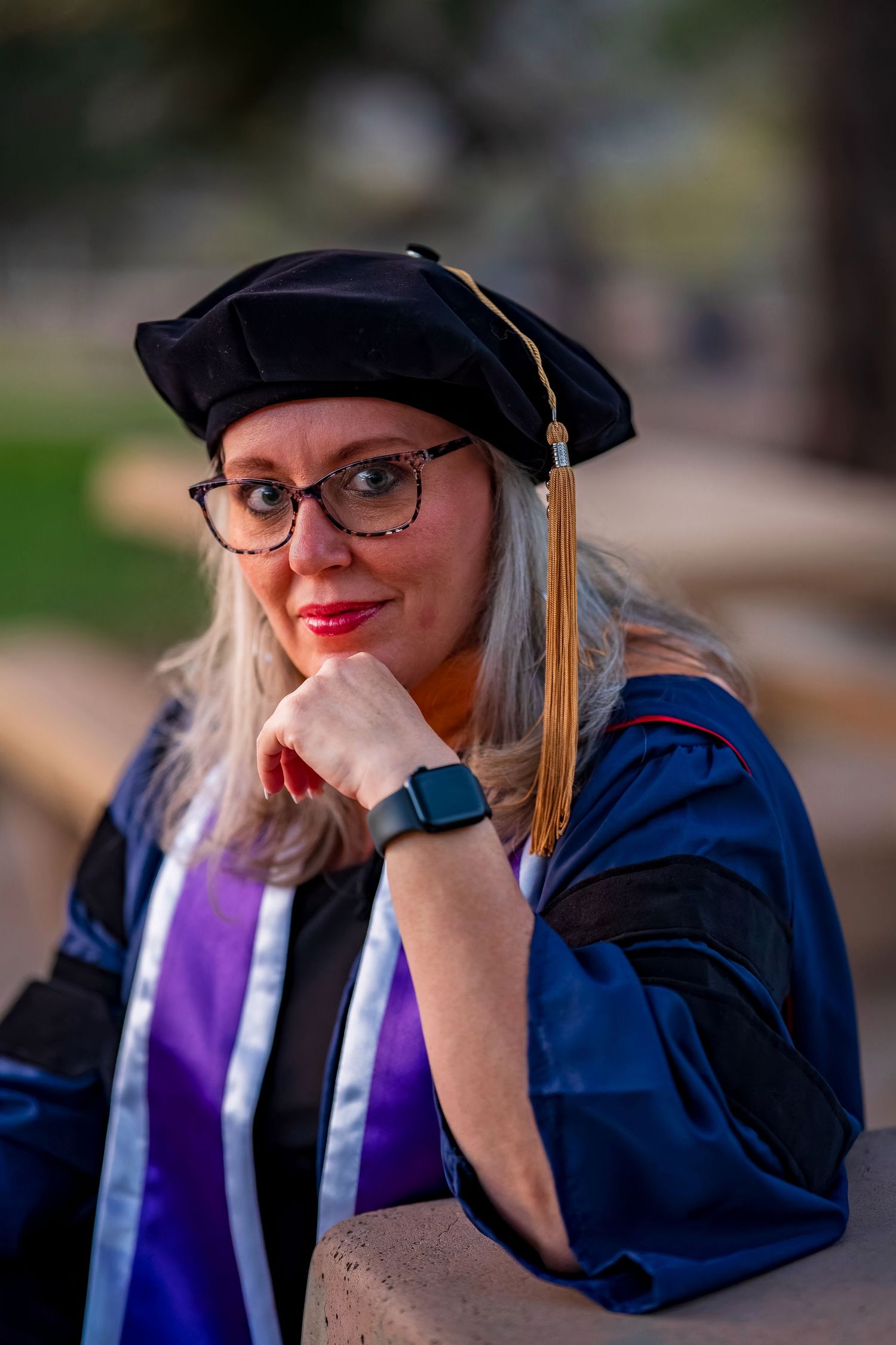 Graduate wearing blue academic regalia and cap poses with joyful expressions during outdoor photo session.