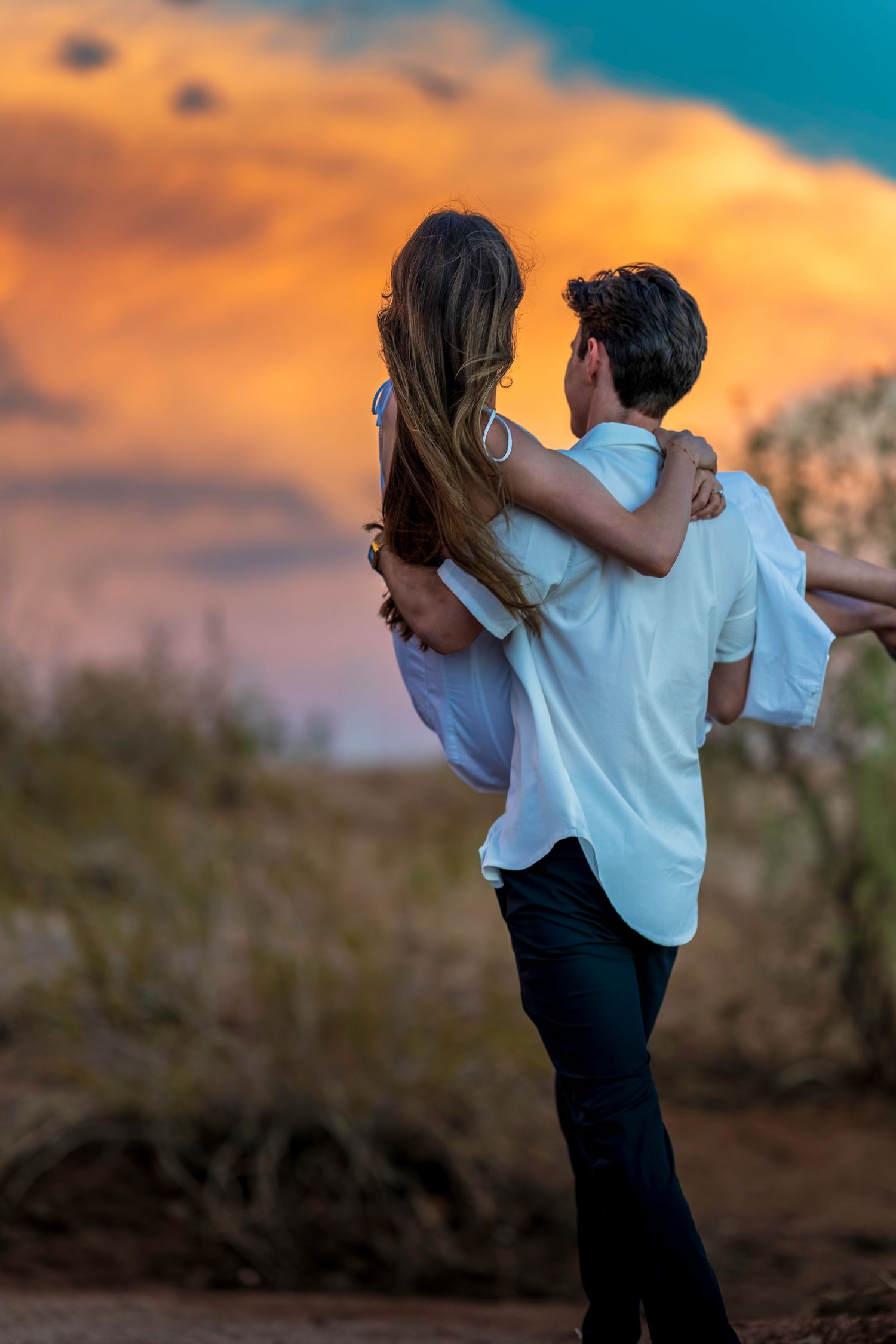 Silhouetted couple embracing on a hill against a colorful sunset sky.