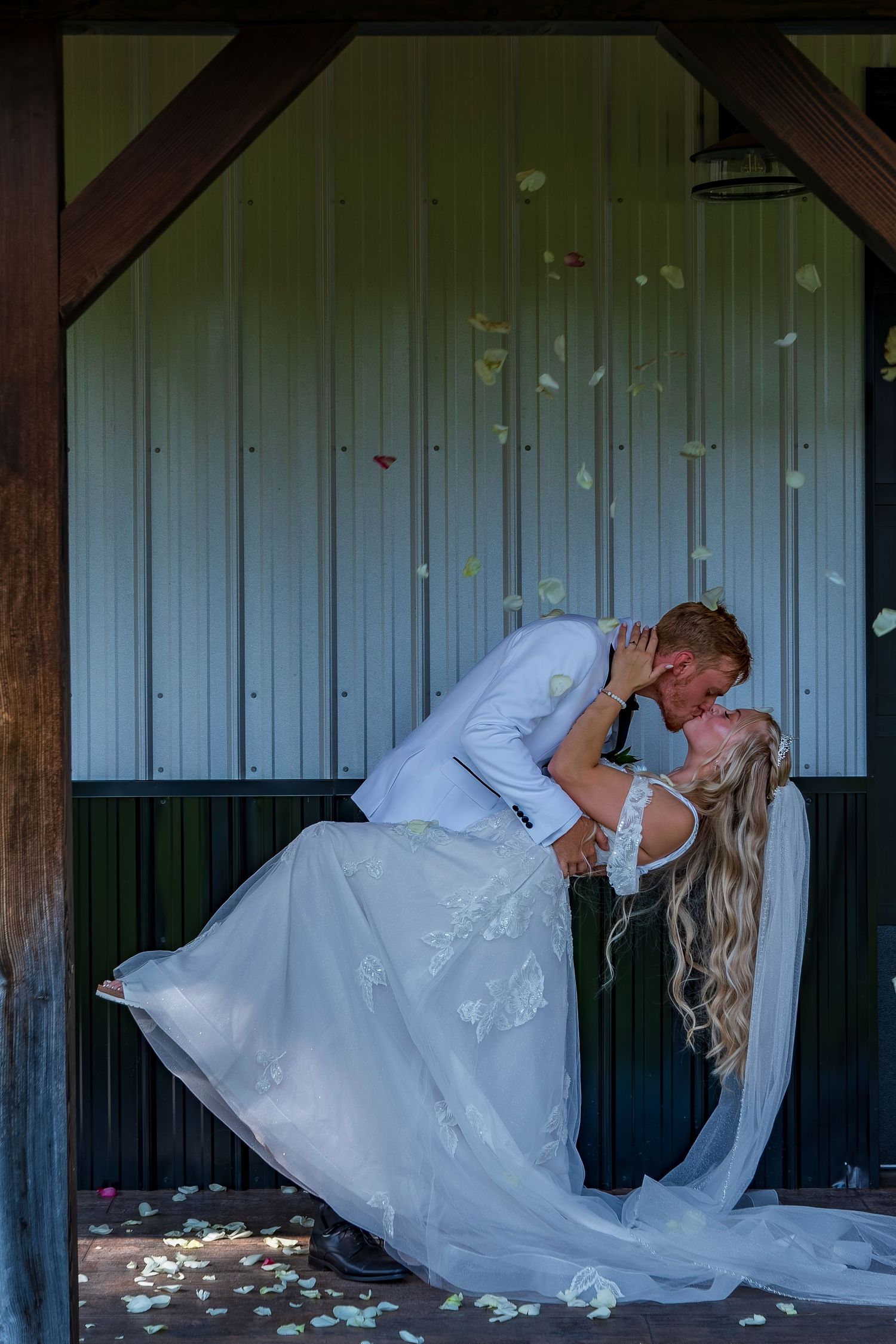 Dramatic wedding dance dip with rose petals falling in rustic barn setting.
