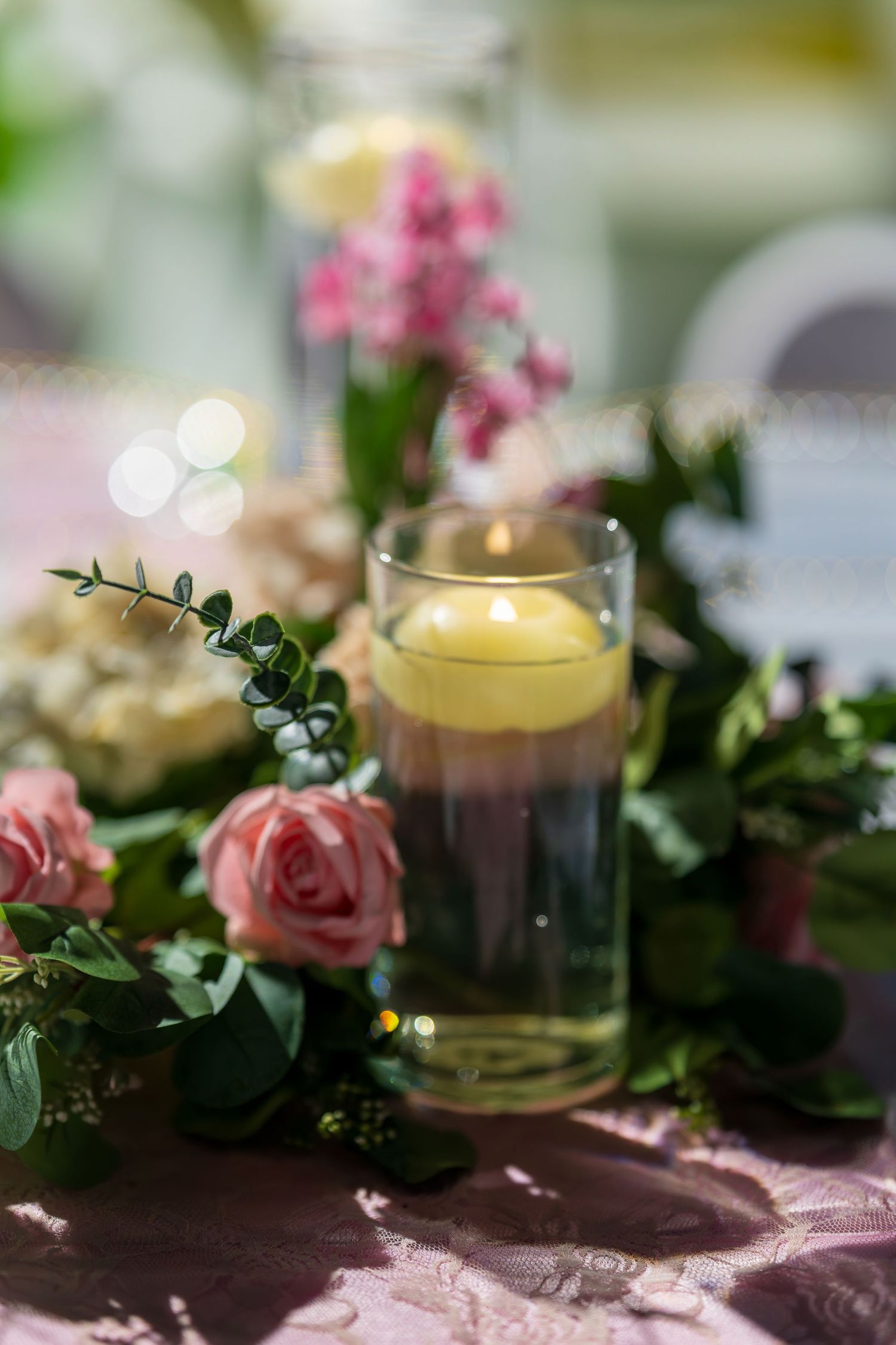 Close-up of romantic table centerpiece with roses, greenery and glowing candles.