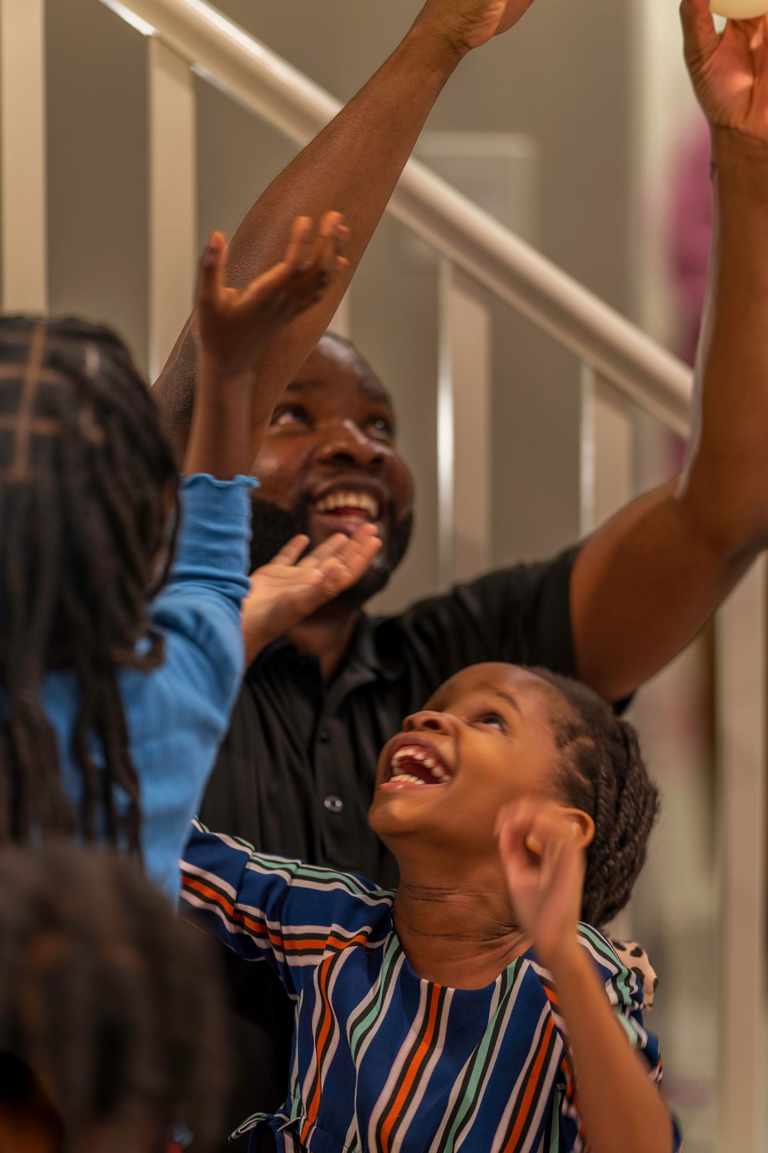 A joyful Black man and child laugh with arms raised in celebration indoors.