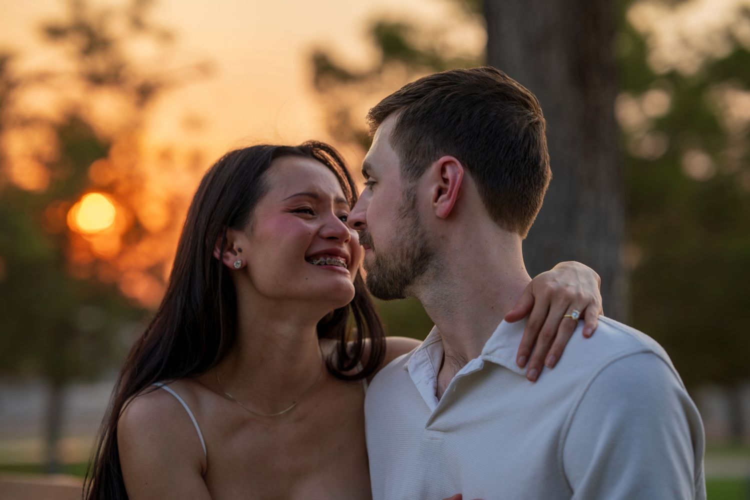 Romantic couple sharing a tender moment at sunset, woman laughing as man kisses her cheek.
