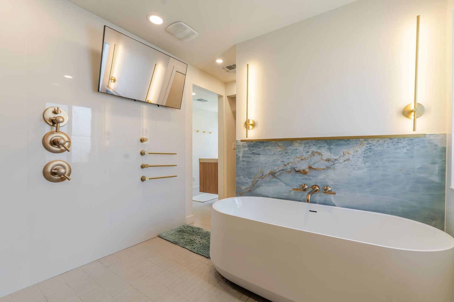 Luxurious modern bathroom with freestanding soaking tub, gold fixtures, decorative wall mural, and wall-mounted TV.