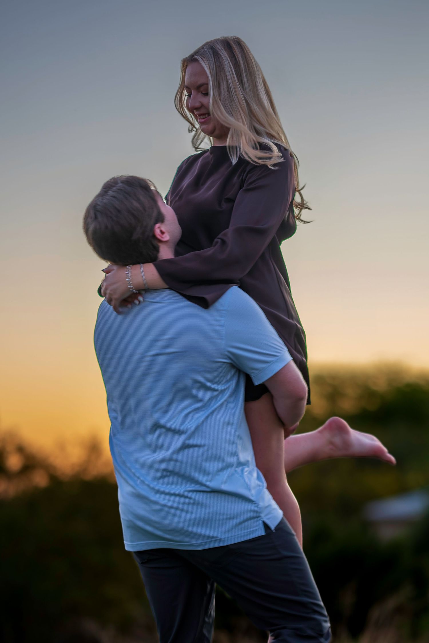 Man lifting woman in his arms during a romantic golden hour sunset engagement photo session.