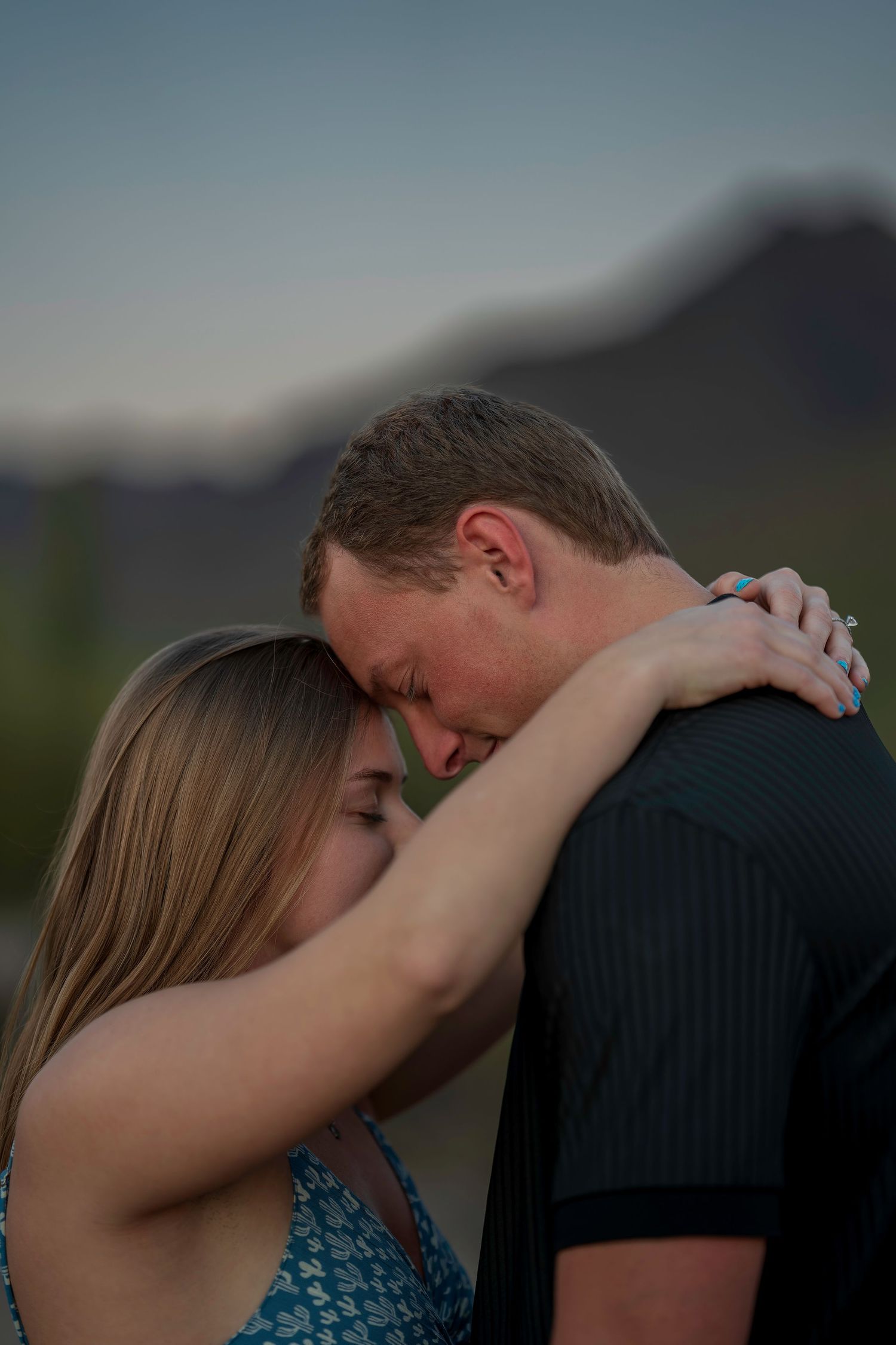 Engaged couple embracing forehead to forehead with mountain twilight background.