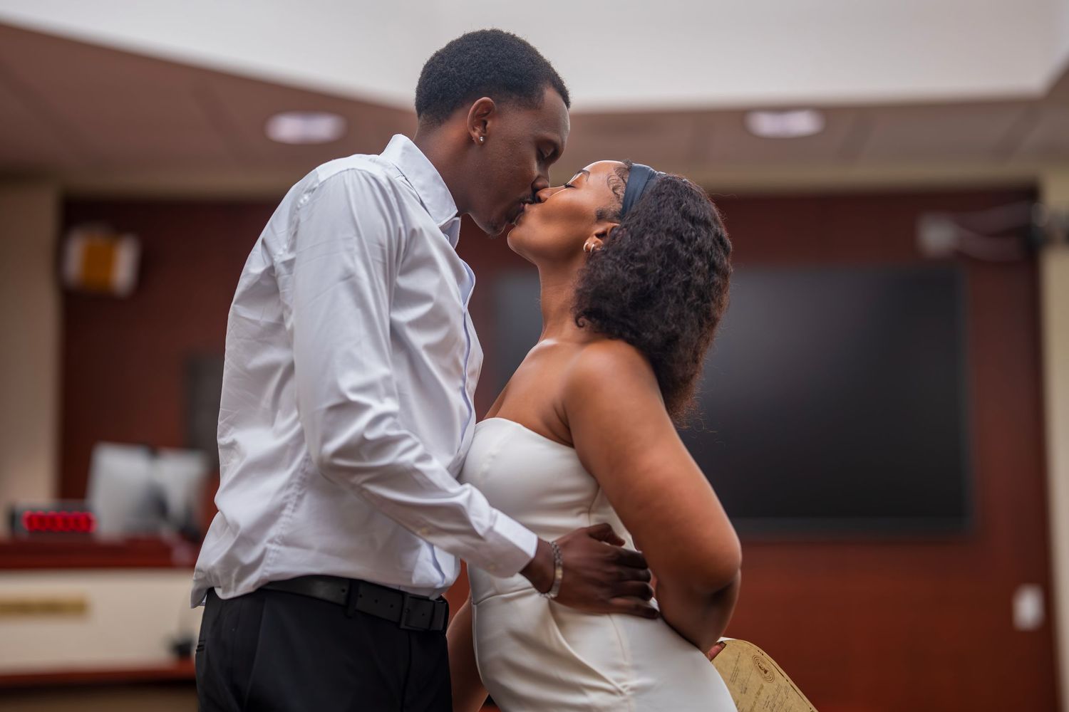 A couple shares a romantic kiss indoors during what appears to be a wedding ceremony.