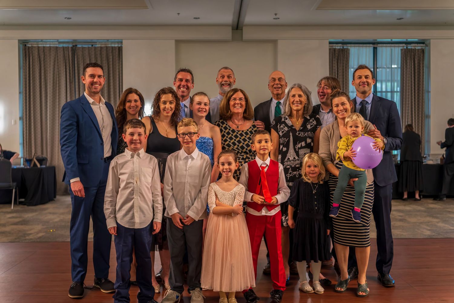 Large family group portrait at formal event with adults and children smiling together in elegant venue.