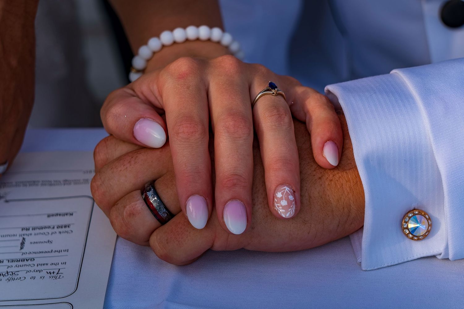 Close-up of hands wearing wedding rings and pearl bracelet during ceremony.