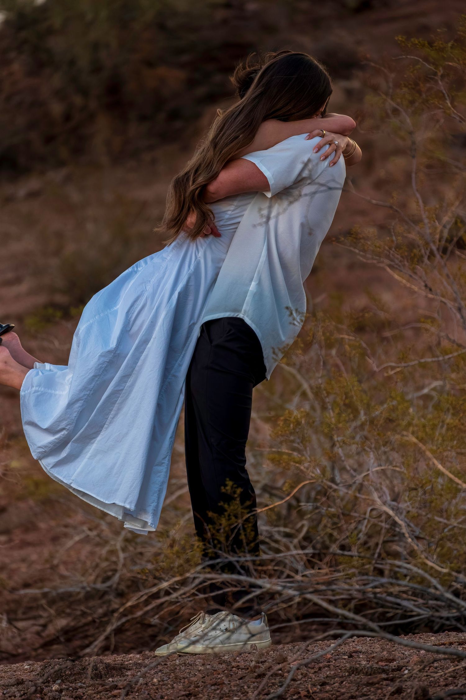 Couple in white dress and casual wear share an intimate dance pose on rocky terrain.