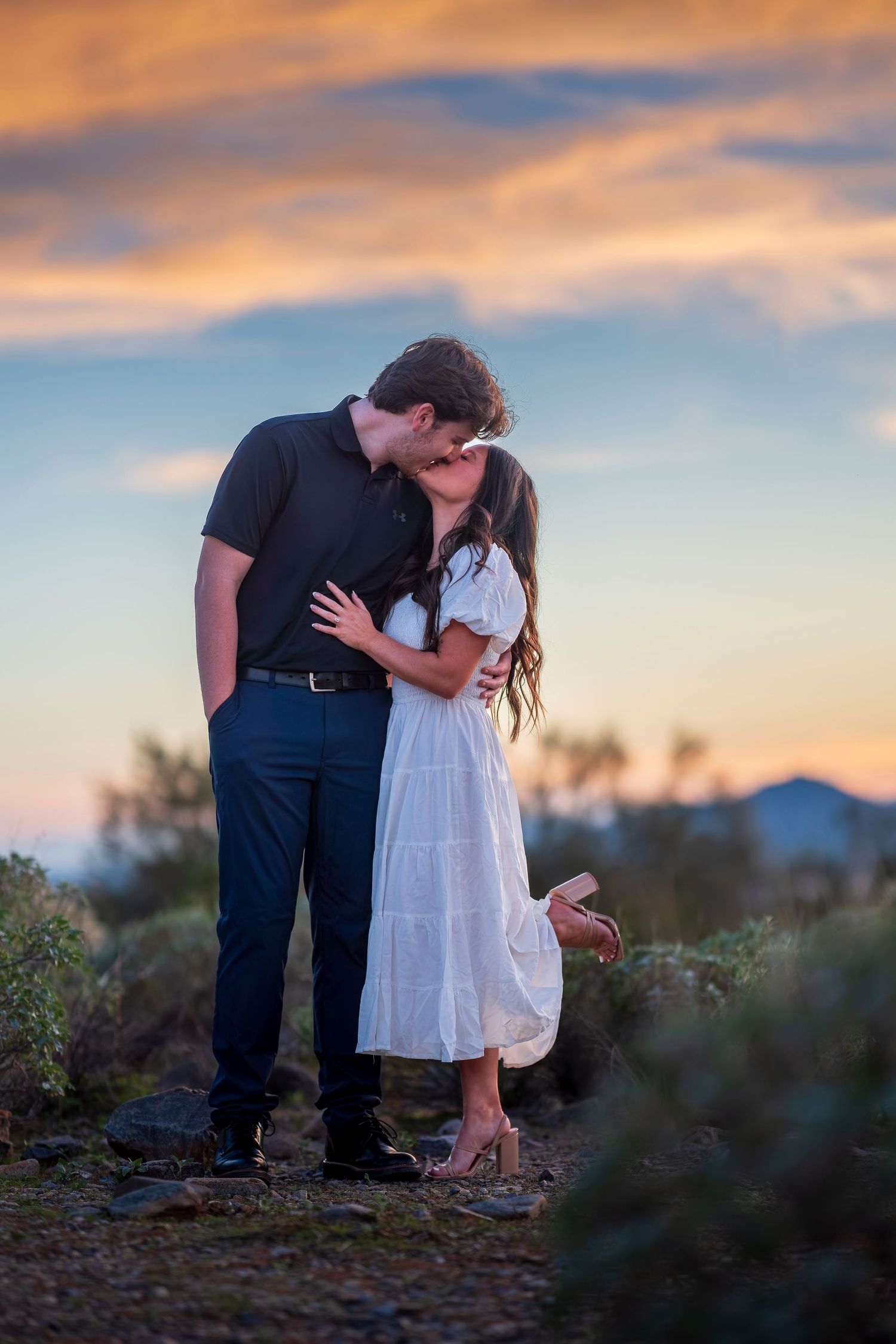 A couple shares an intimate moment against a colorful desert sunset backdrop.