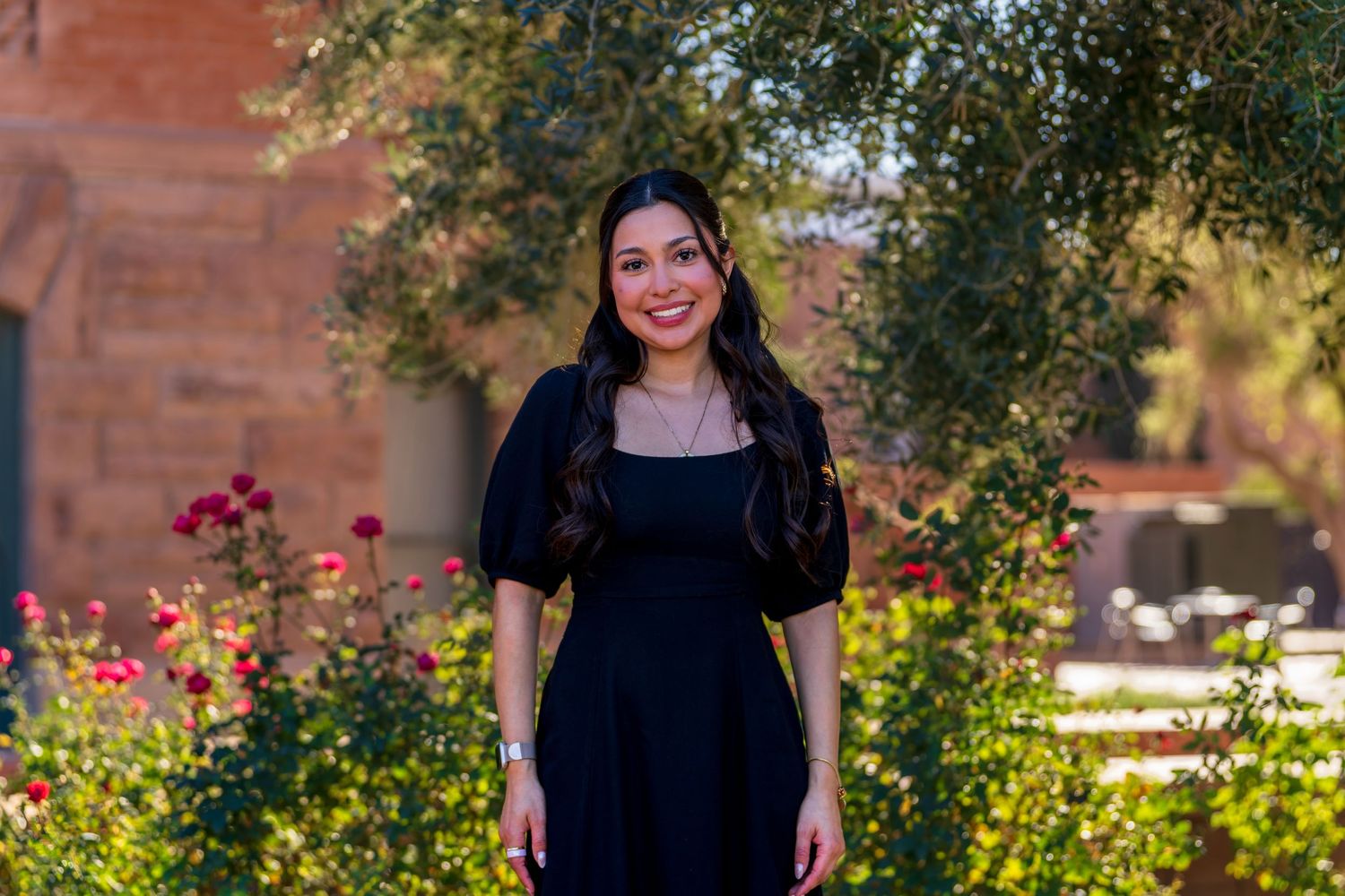 Portrait session in garden setting with brick building and trees in background.
