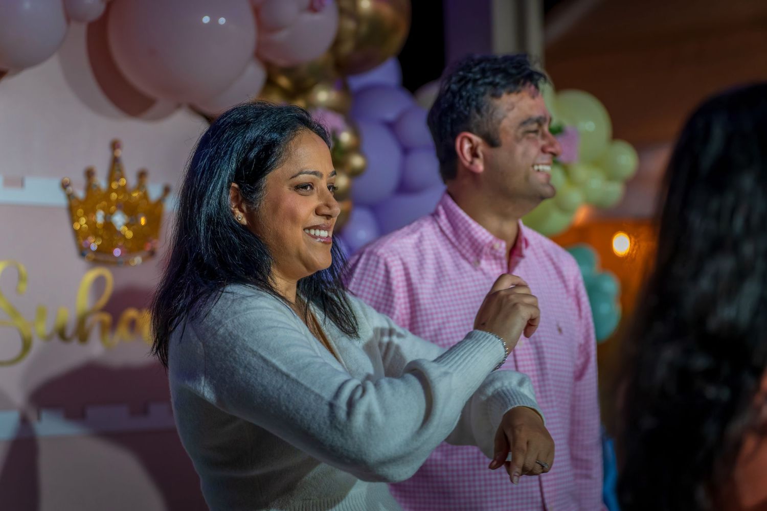 People celebrating at an indoor party with decorative balloons and warm lighting.