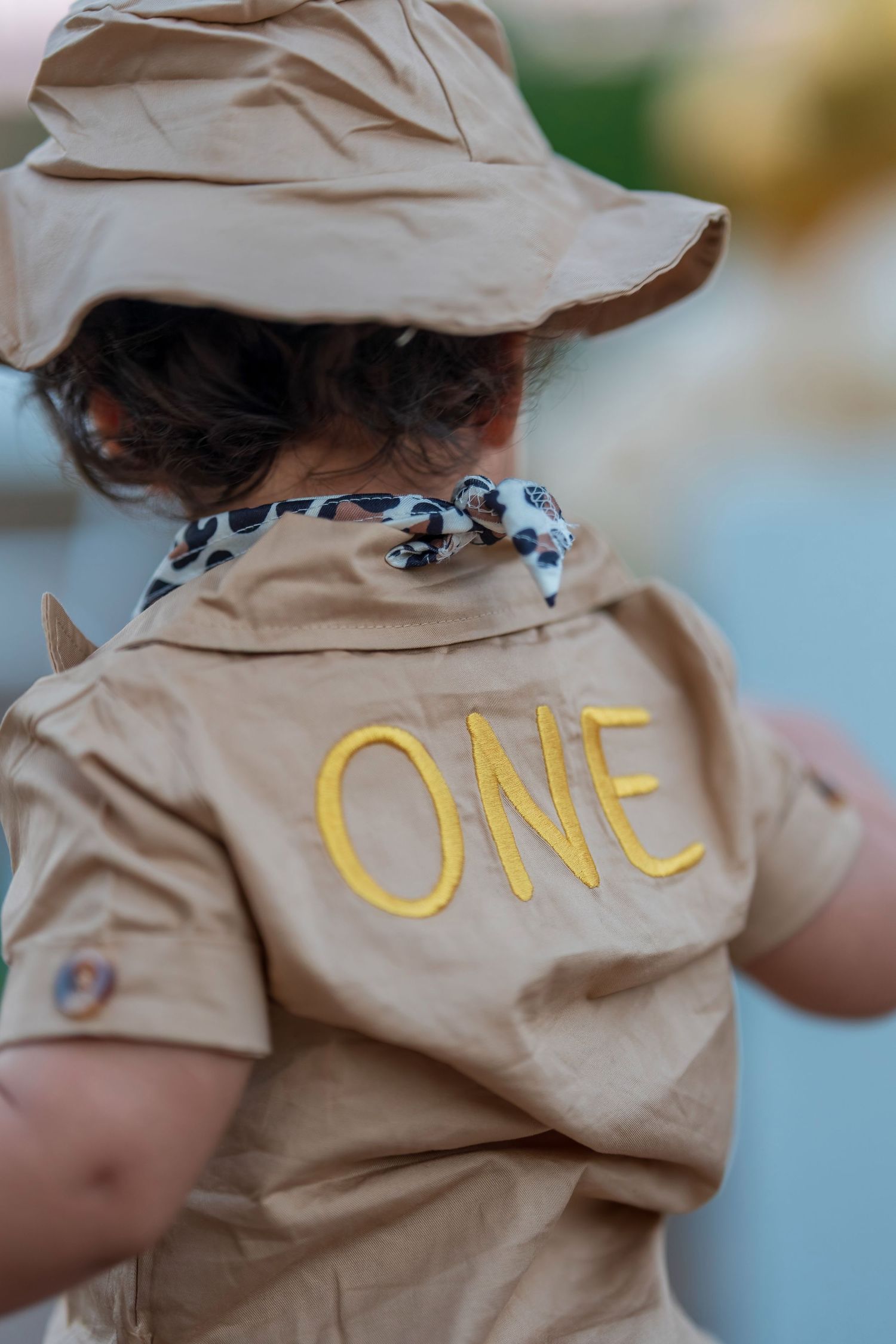Back view of tan safari costume showing yellow 'ONE' embroidery and matching hat.