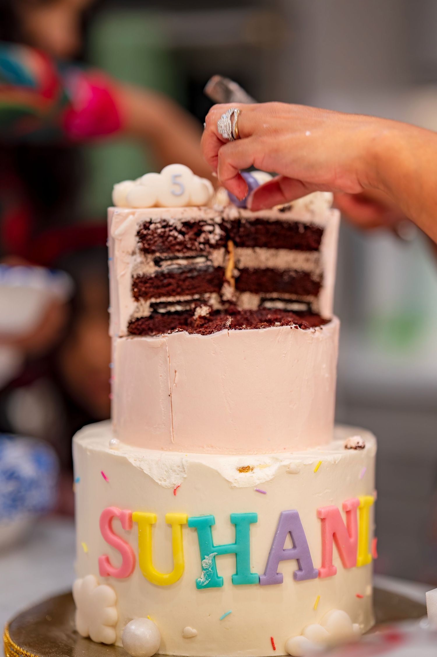 A white frosted birthday cake with colorful lettering and chocolate layers being cut.
