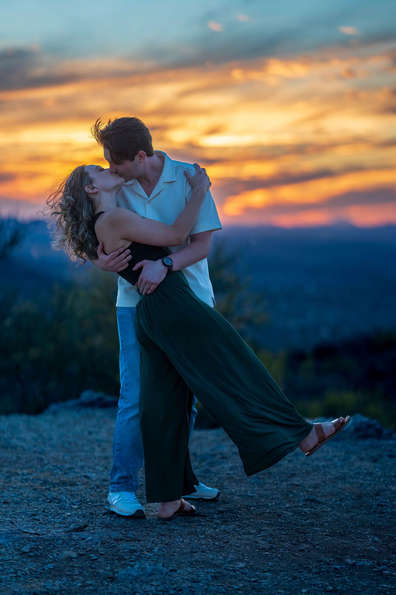 Couple shares romantic kiss at sunset with vibrant orange and blue sky over desert landscape.