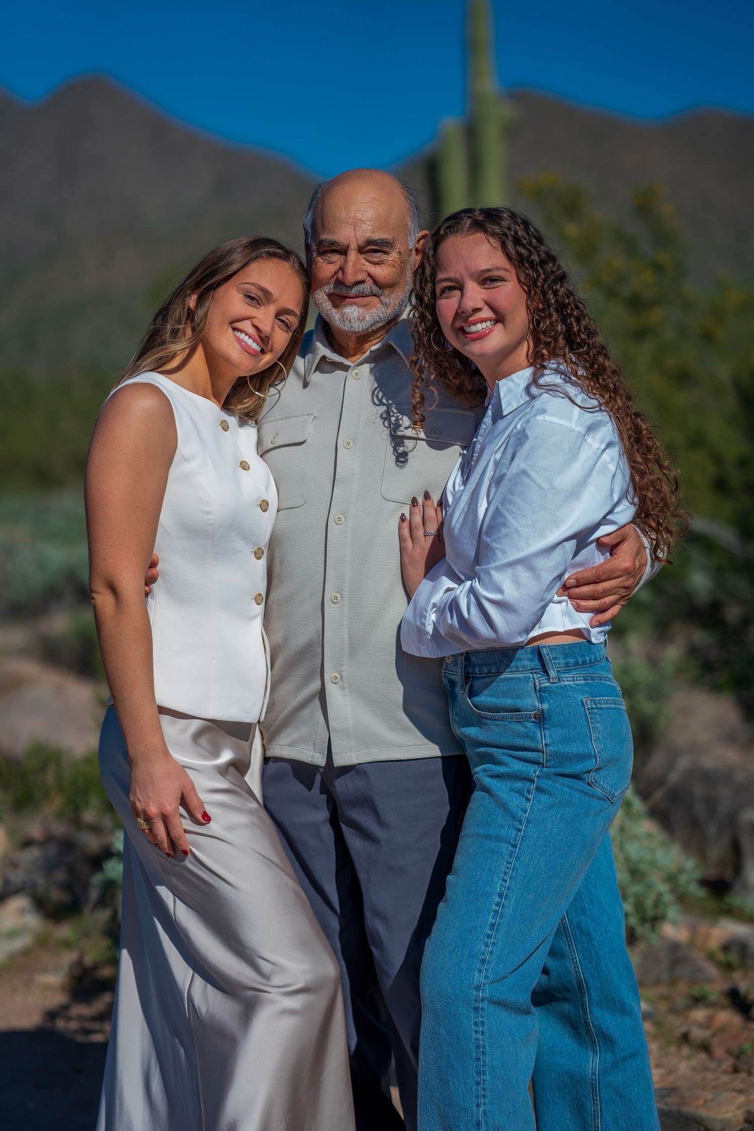 Three people share a warm embrace while posing for a photo in the desert.