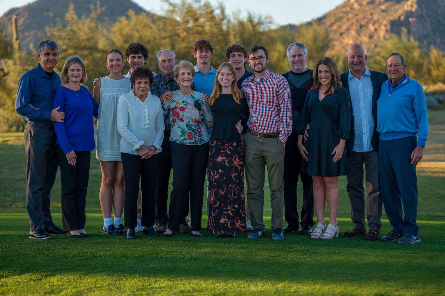 Large family gathering posed together on grass with mountain vista behind them.
