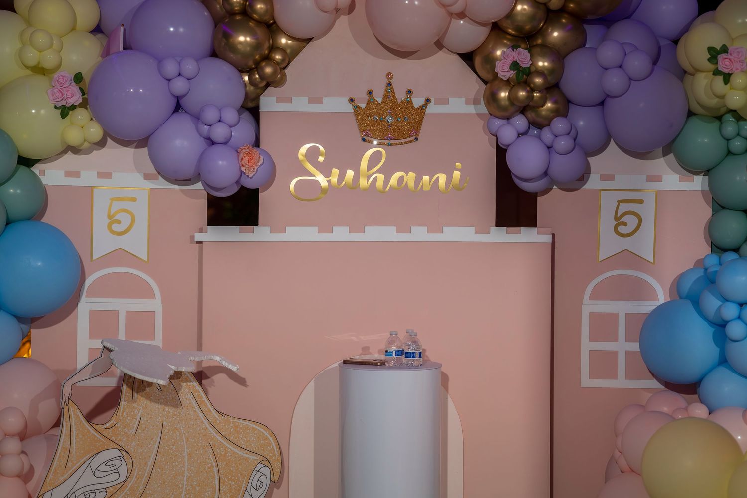 Pastel balloon arch decorations with gold crown accent at a party venue.