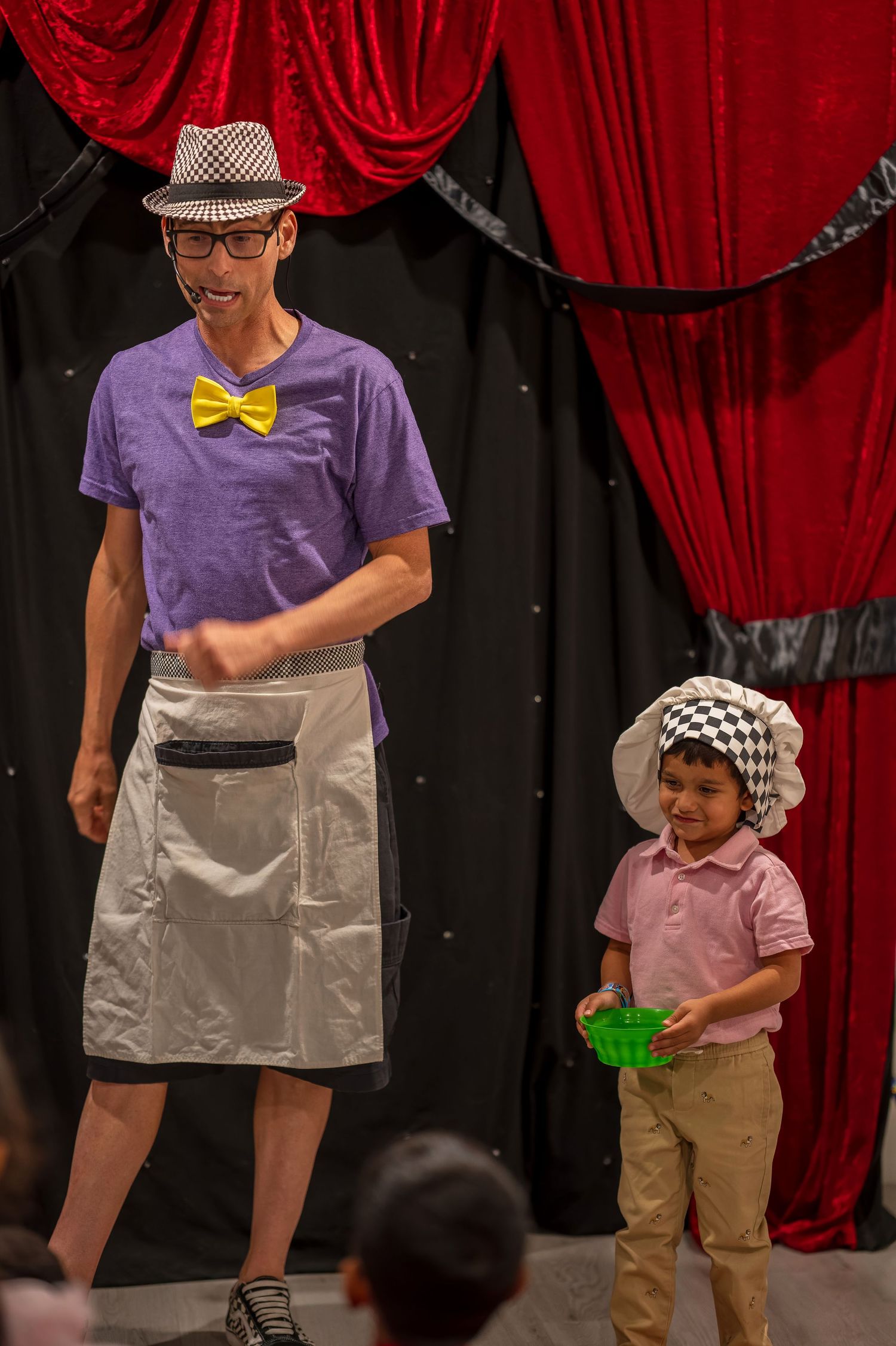 A magic show performance on stage with red curtains featuring colorful props and costumes.