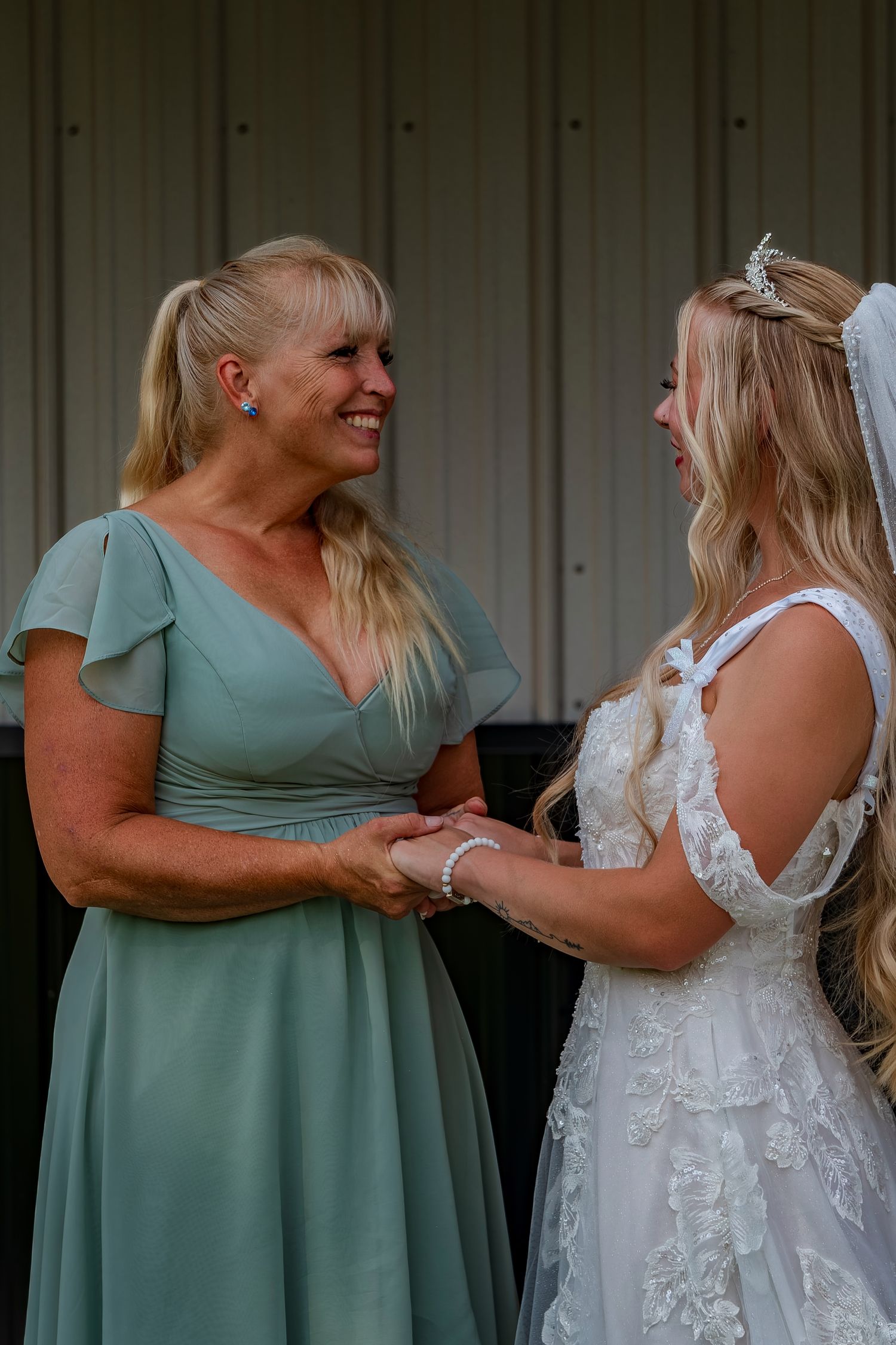 Bridesmaids in sage green dresses share joyful moments with the bride in her lace gown.