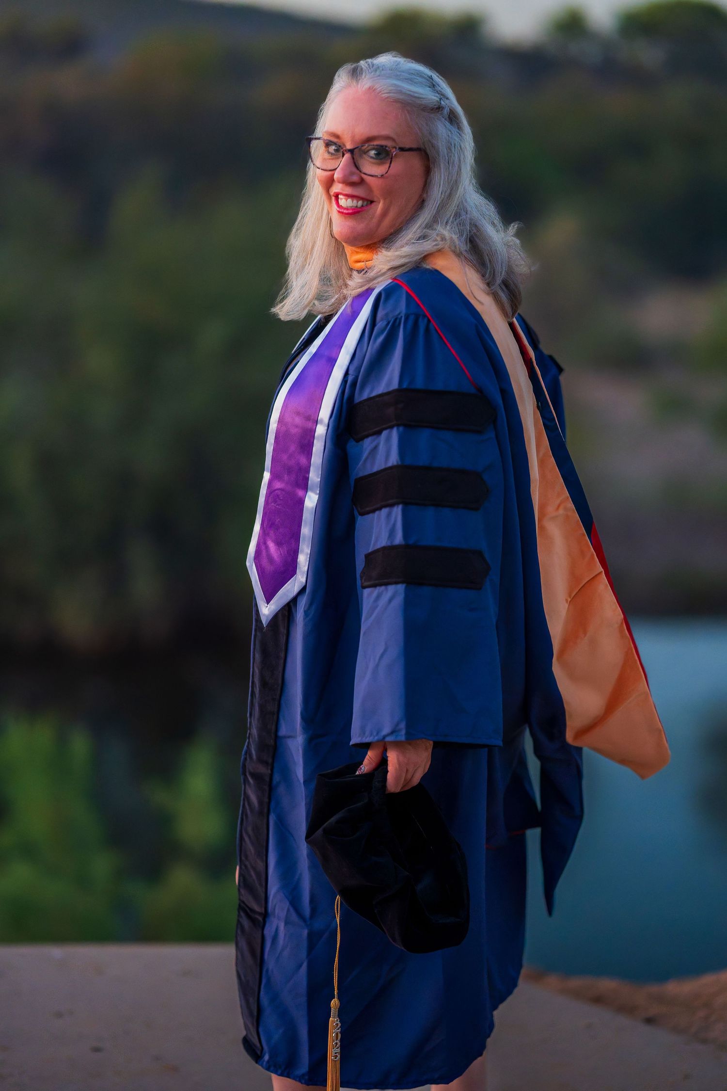 Academic regalia with blue gown and purple stole captured in outdoor setting.