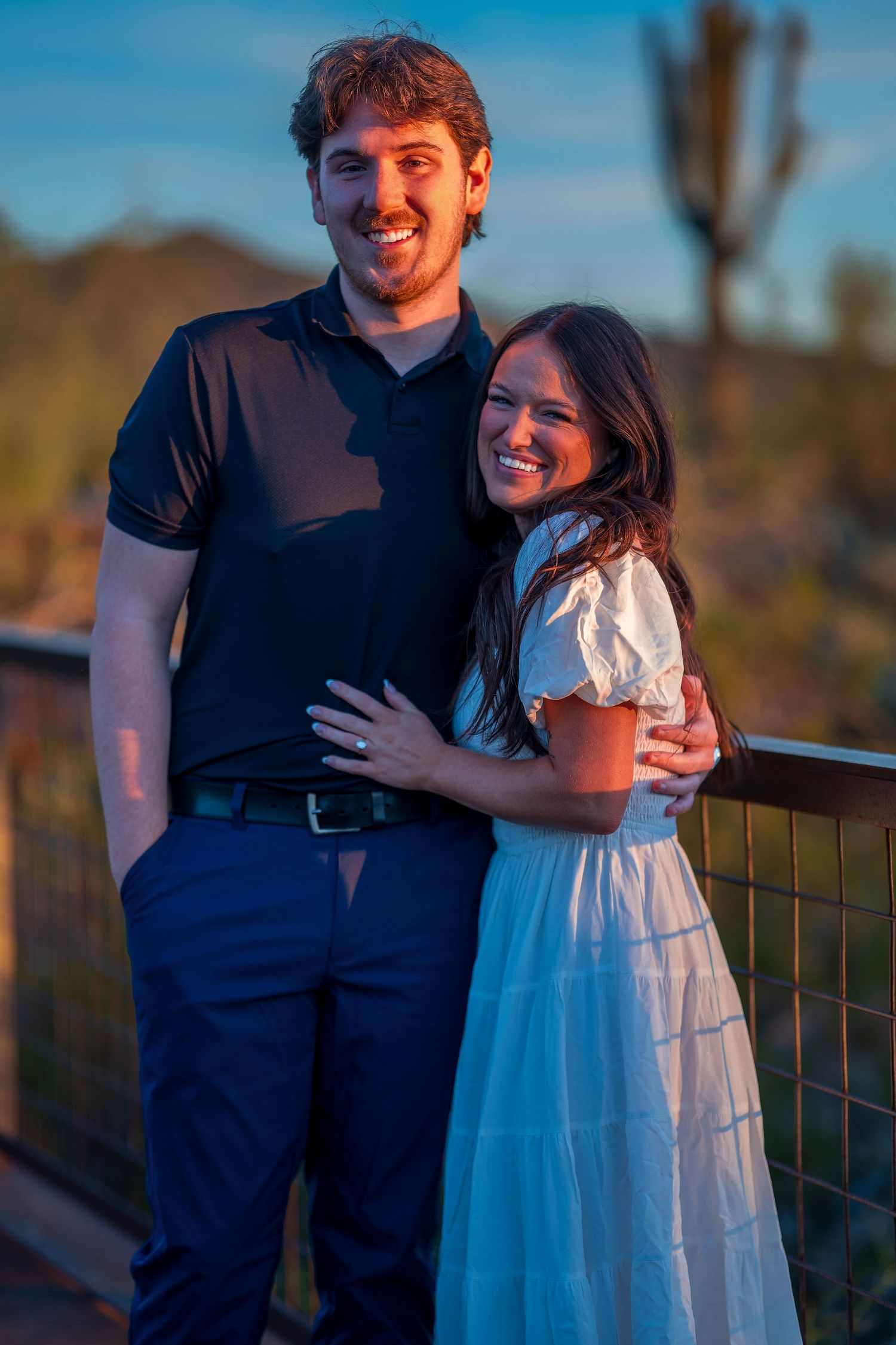 A romantic sunset photoshoot showing a couple embracing on a deck with desert mountains in the background.
