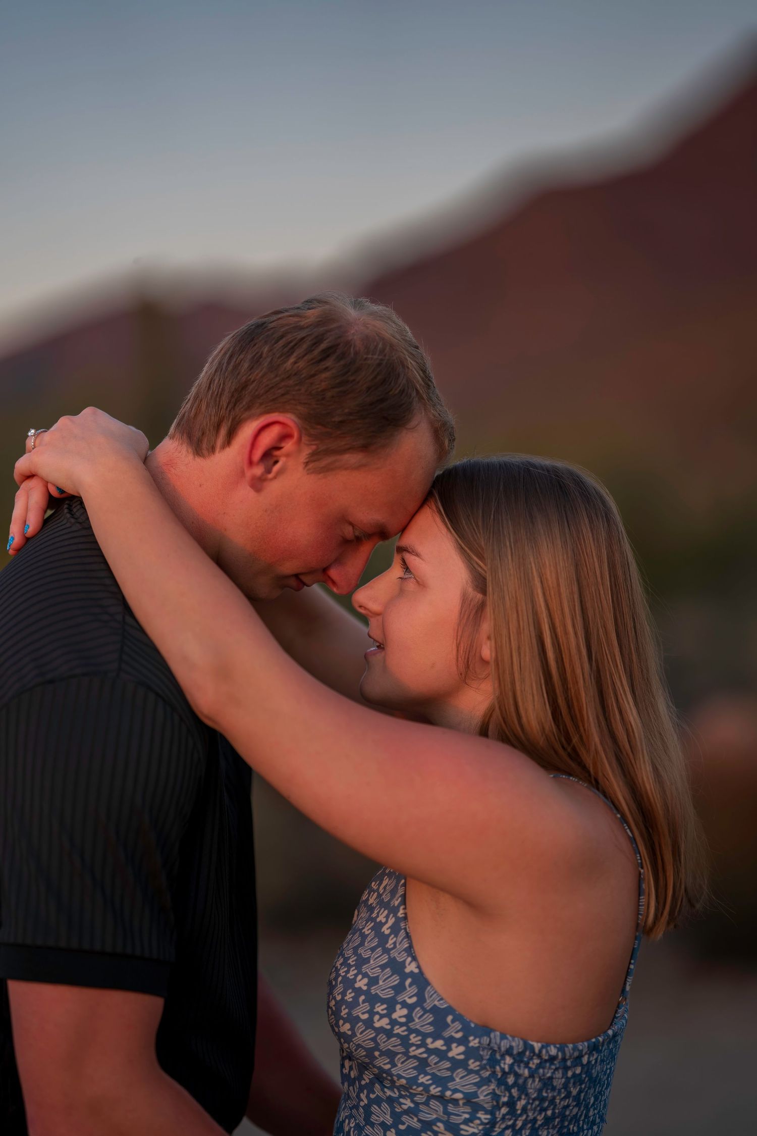 Romantic couple touching foreheads at sunset with mountain backdrop in warm golden light.