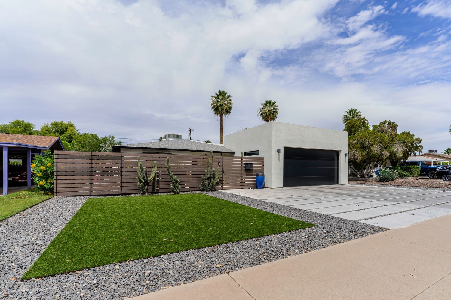 Modern home exterior with manicured lawn, wood fence, white stucco walls, and two-car garage in sunny Arizona.
