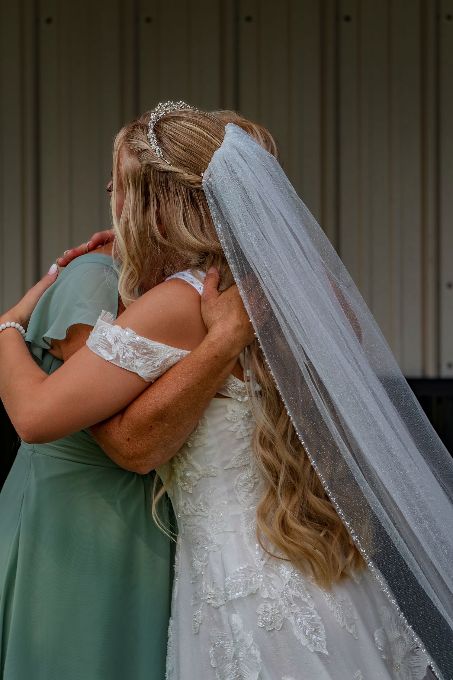 Candid wedding moment showing two women hugging with one in sage green and one in white lace.