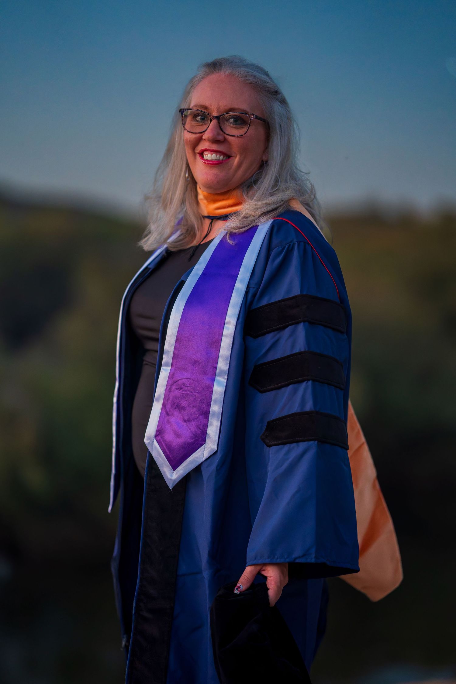 Academic regalia with purple stole and blue gown photographed at sunset.