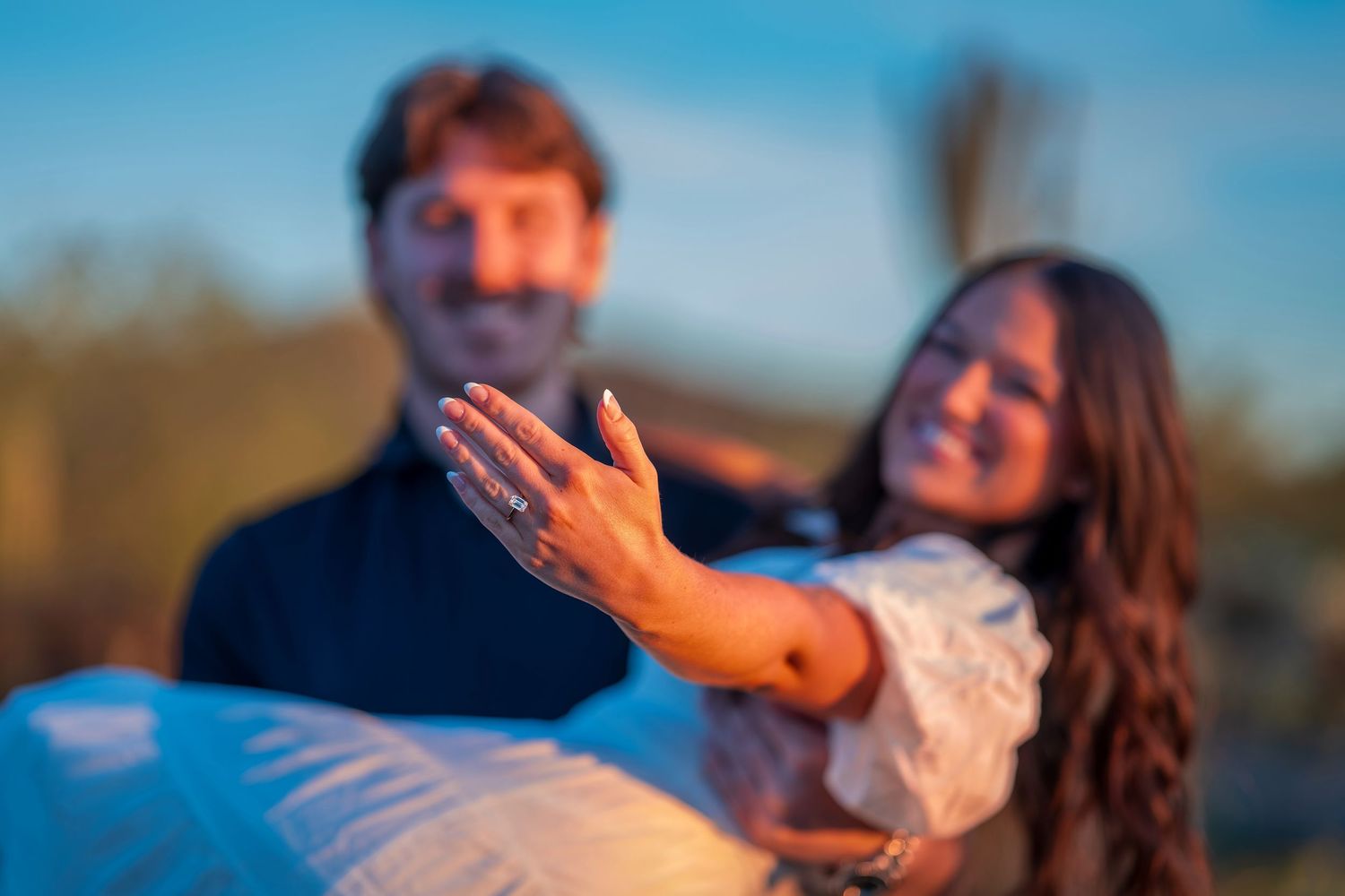 Joyful couple sharing a playful moment while posing against a desert backdrop at sunset.