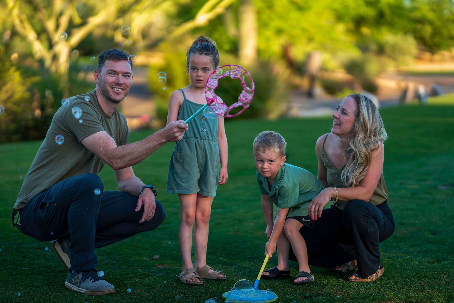 Family with two kids making bubbles together on green grass in a park.