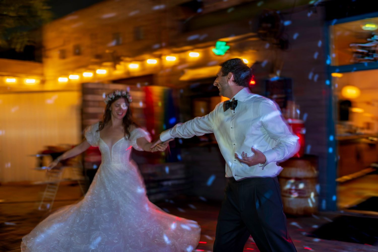 Bride and groom share a romantic first dance outdoors at night with string lights and confetti.