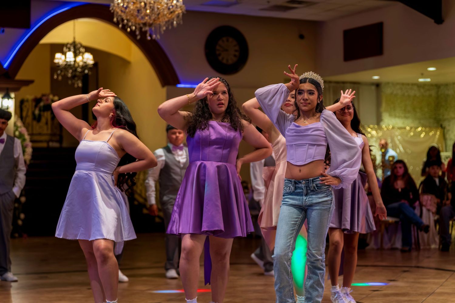 Young women in purple dresses perform a choreographed dance routine at an elegant indoor event venue.