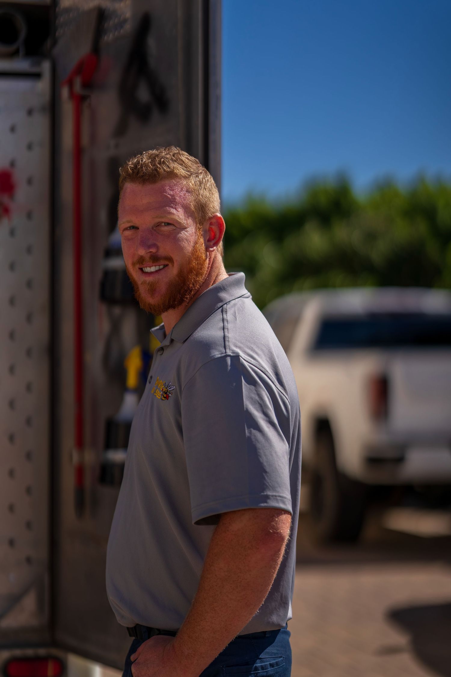 Professional service technician in grey uniform standing outdoors on sunny day.