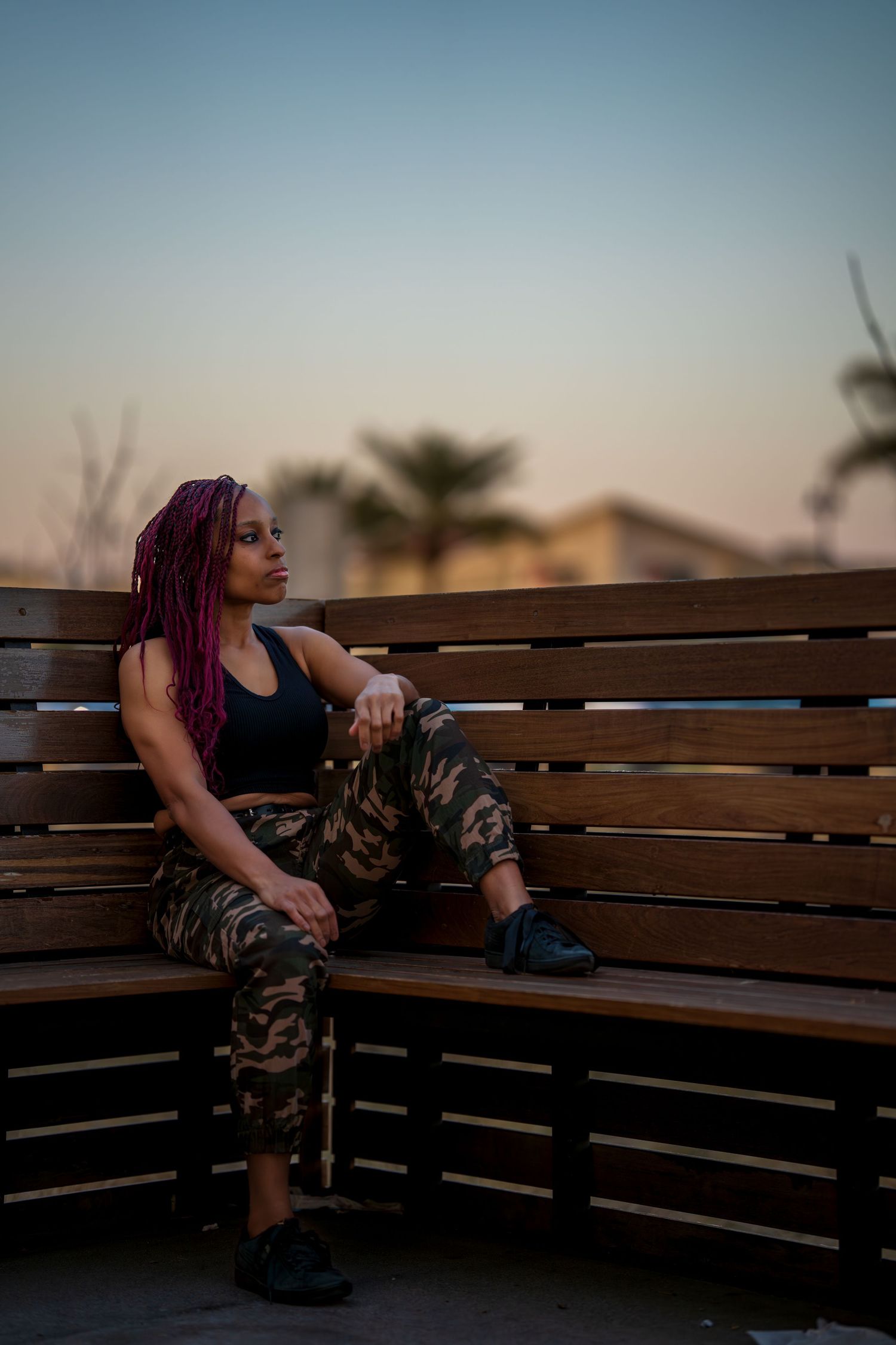 Relaxed pose on a wooden bench during sunset with urban background.