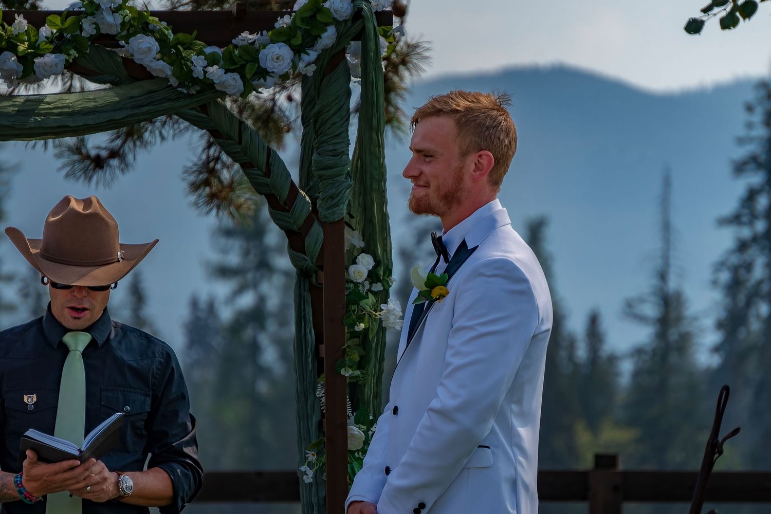 Wedding attendees gather under a wooden arch during a mountain ceremony.