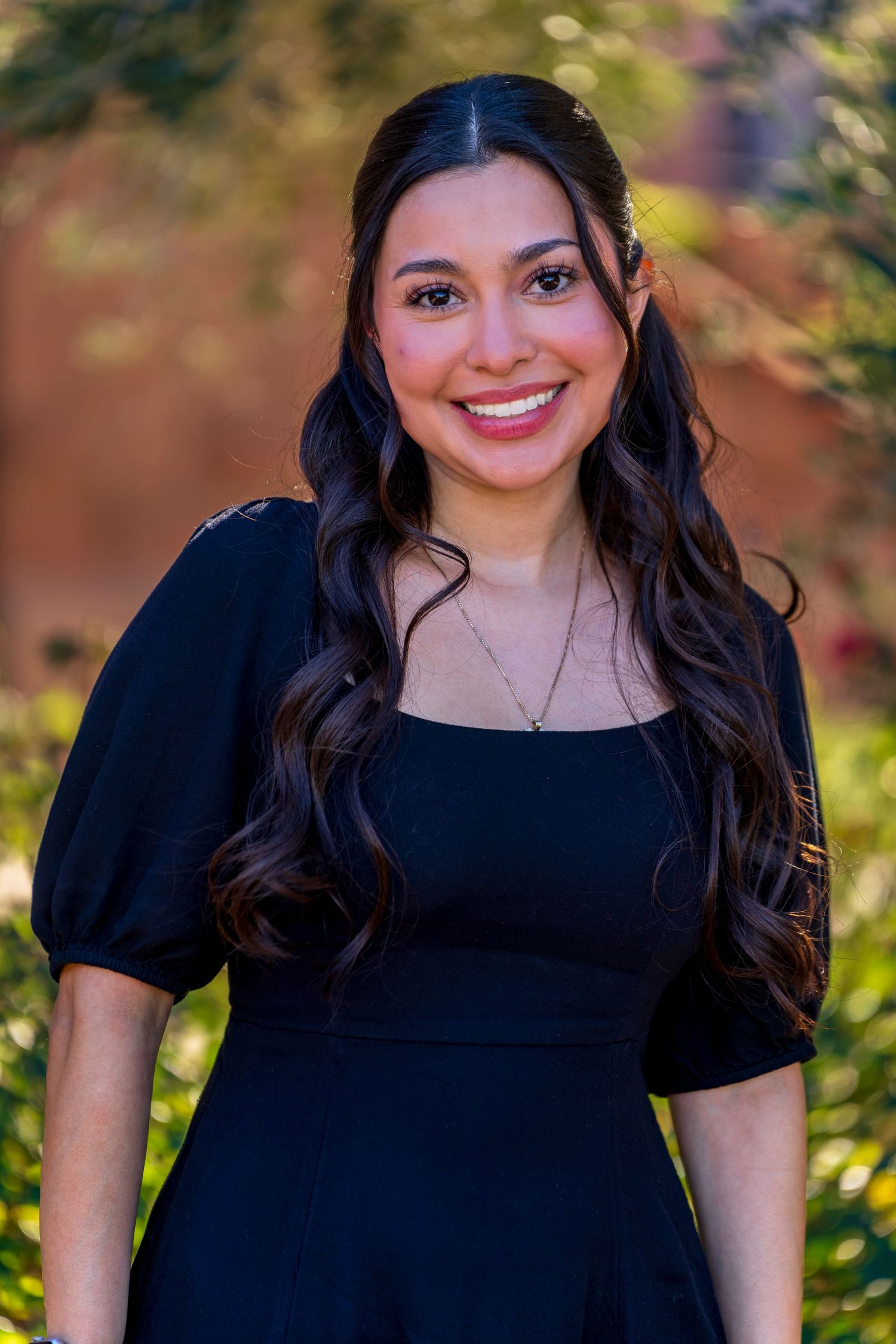 Outdoor portrait with natural lighting against backdrop of trees and flowers.