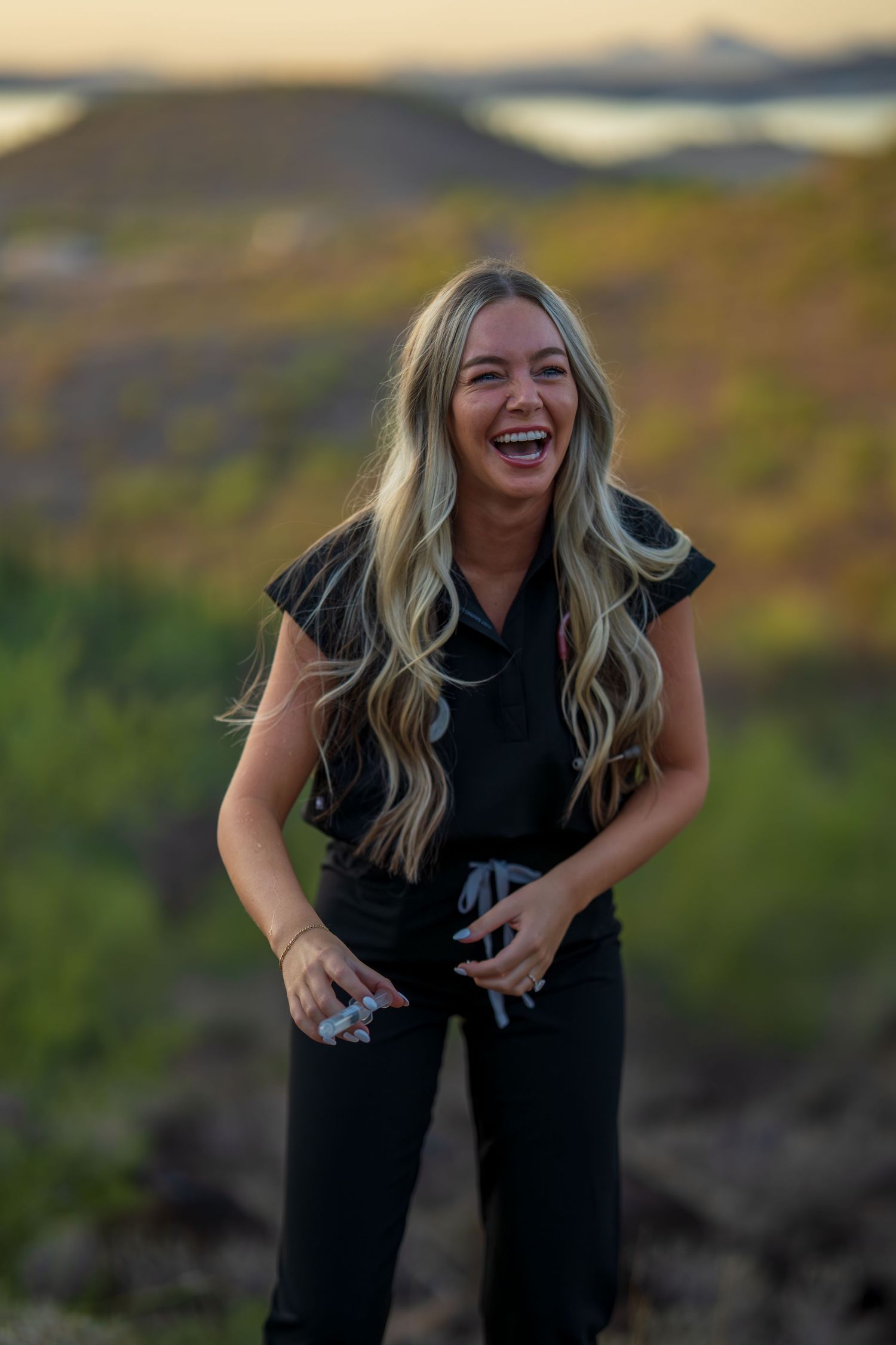 Medical professional in dark scrubs shares genuine laughter during sunset desert photoshoot.