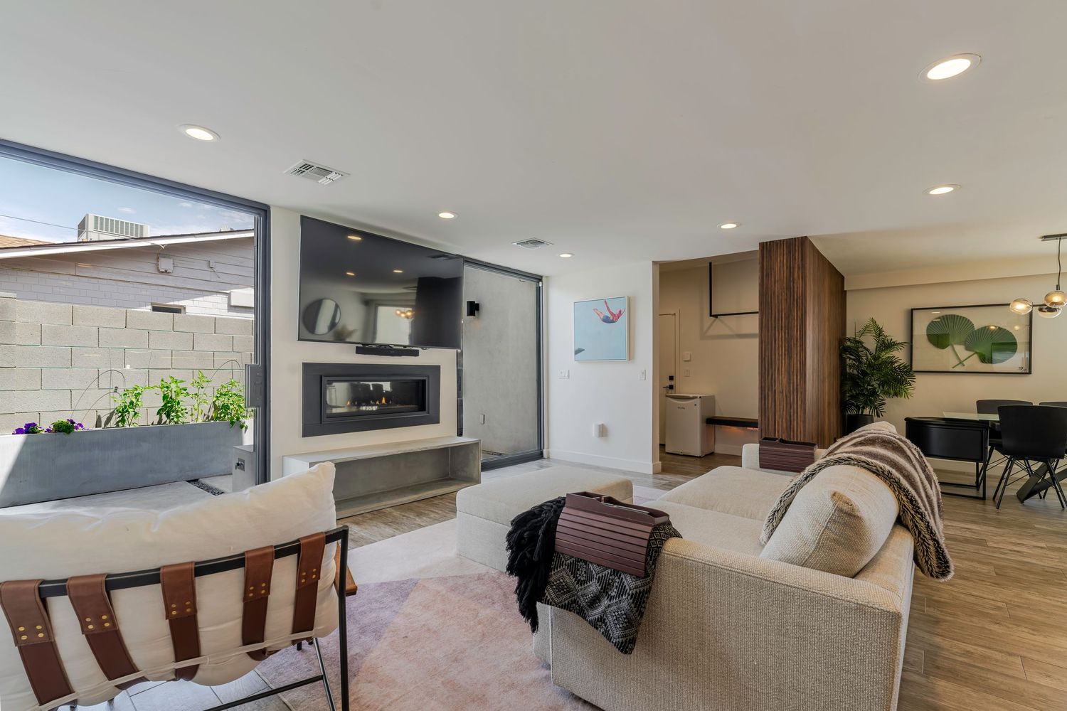 Modern open-plan living room with sofa, fireplace, recessed lighting, and seamless indoor-outdoor patio access.