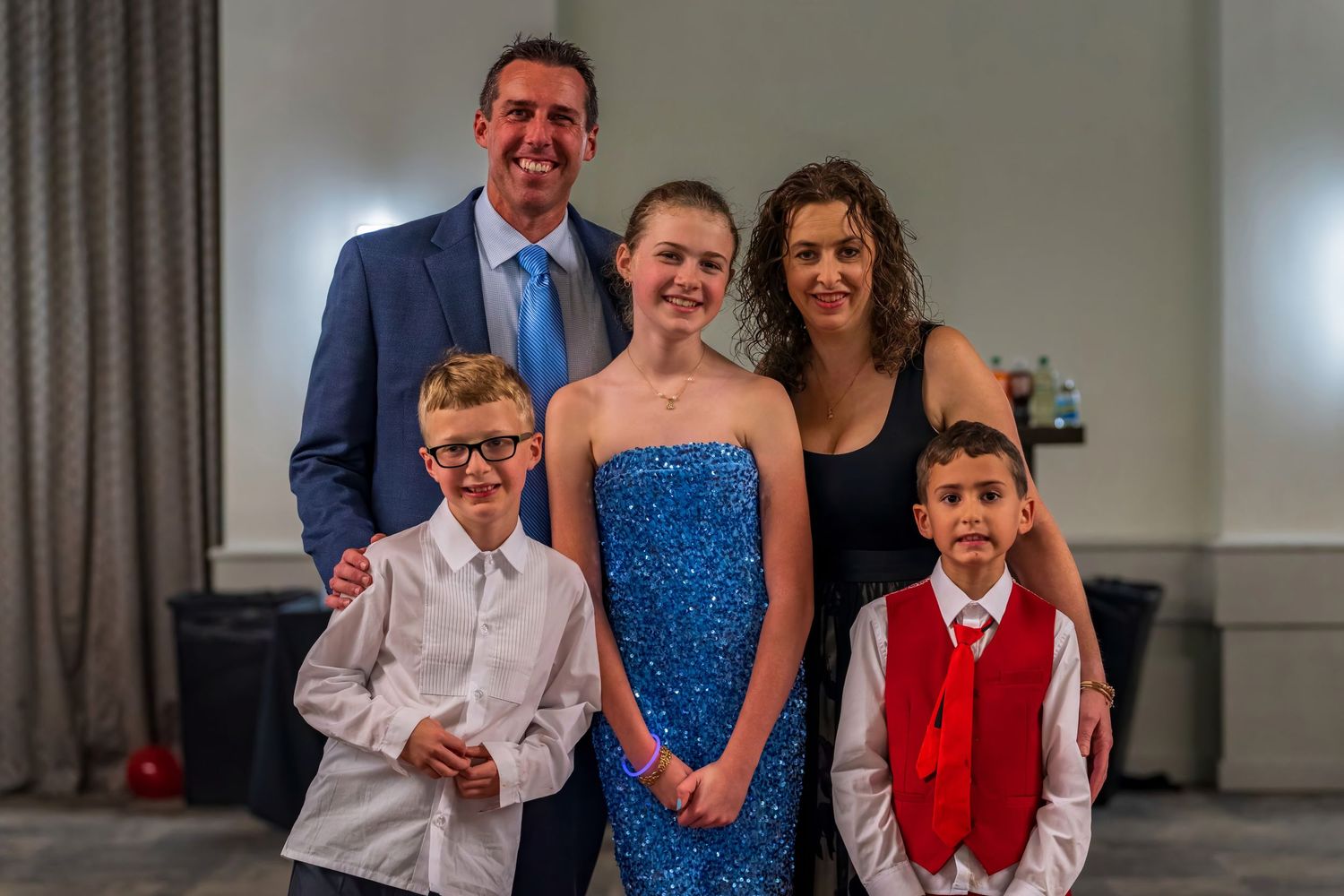 Family of five posing together at a formal event, parents with two boys and a teenage girl in a blue sequin dress.