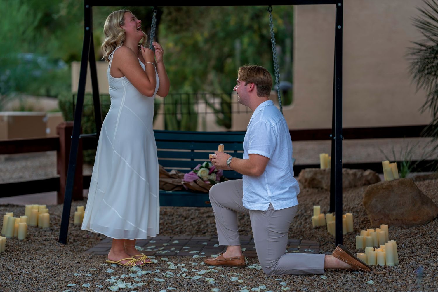 Romantic outdoor marriage proposal with man kneeling holding ring box for emotional woman.