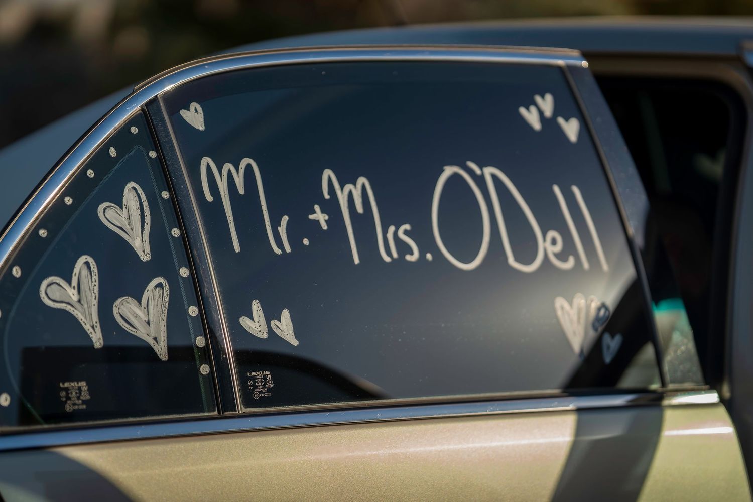 Car window decorated with Mr. and Mrs. O'Dell written in white with hand-drawn hearts for wedding getaway.