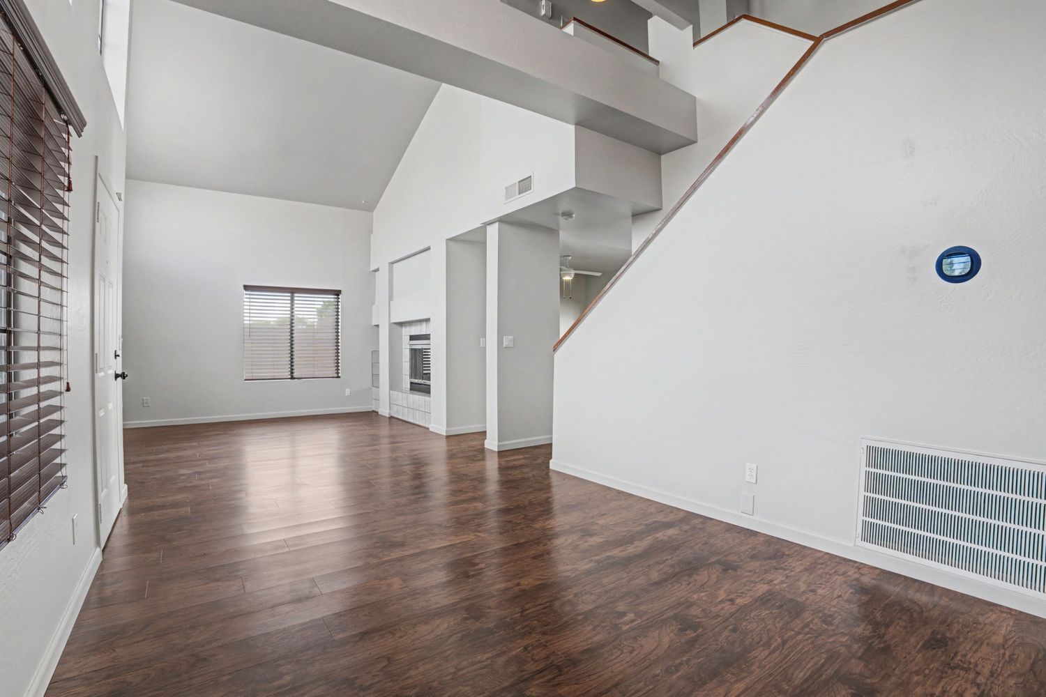 Spacious open living area with dark hardwood floors, high vaulted ceilings, and staircase in a modern home.